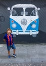 A boy in the shape of a Barcelona FC near a graffiti painting of a Volkswagen bus painted on a wall.