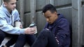 Boy sharing warm coffee with frozen homeless teenager, charity volunteer