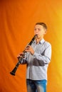 Boy in shirt and jeans plays the clarinet on a yellow background