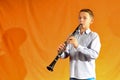 Boy in shirt and jeans plays the clarinet on a yellow background