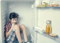 A boy in a shirt and shorts eating a chocolate bar inside an open fridge with food Royalty Free Stock Photo