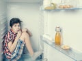 A boy in a shirt and shorts eating a chocolate bar inside an open fridge with food Royalty Free Stock Photo