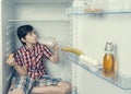 A boy in a shirt and shorts eating a croissant and drink milk inside a fridge with food and product. Close-up