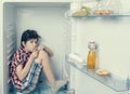 A boy in a shirt and shorts licking one`s fingers inside an open fridge with food remains Royalty Free Stock Photo