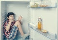 A boy in a shirt and shorts licking one`s fingers inside an open fridge with food remains Royalty Free Stock Photo