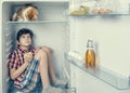 A boy in a shirt and shorts with red cat looking at each other inside a fridge with food and product. Close-up Royalty Free Stock Photo