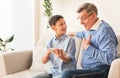 Boy Showing Grandfather How To Play On Smartphone Sitting Indoor