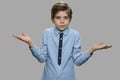 Boy shrugging shoulders against gray background.