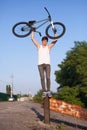 The boy with silver bike overhead standing on an iron pole