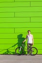 Boy with silver bike stay at green wall background