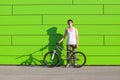 Boy with silver bike stay at green wall background