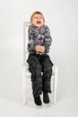 The boy sits and grimaces on a chair on a white background Royalty Free Stock Photo