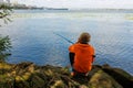 the boy sits with his back and catches fish with a fishing rod in the river Royalty Free Stock Photo