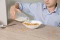 A boy sits in the kitchen and pours milk into cornflakes. Royalty Free Stock Photo