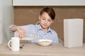 A boy sits in the kitchen and pours milk into cornflakes. Royalty Free Stock Photo