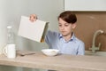 The boy sits in the kitchen at the table and prepares a breakfast of milk Royalty Free Stock Photo