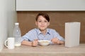 The boy sits in the kitchen at the table and prepares a breakfast of milk Royalty Free Stock Photo