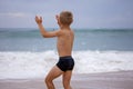 Boy sits on the ocean shore with his arms open towards wind and waves. Storm in summer, courage