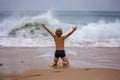 Boy sits on the ocean shore with his arms open towards wind and waves. Storm in summer, courage