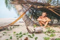 Boy sits in selfmade hut on the tropical beach and plays in Robinzone