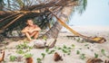 Boy sits in selfmade hut on the tropical beach and plays in Robinzone