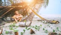 Boy sits in selfmade hut on the tropical beach and plays in Robinzone