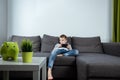 A boy sits on a sofa in the living room and plays with a smartphone. Boy texting on the phone. The concept of harming modern