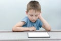 The boy sits at the table and looks at the tablet with interest, concentration and seriousness. Isolated screen for