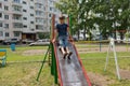 The boy sits at the top of a metal children`s slide and is going to slide down in the courtyard of a residential building Royalty Free Stock Photo