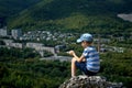 The boy sits on the top of the mountain and enjoys a panoramic view of the verdant valley and the city of Zhigulevsk.