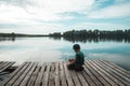 Boy sitting alone on pier while fishing from dock on lake. Kid on beautiful morning in nature Royalty Free Stock Photo