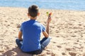 Boy sitting on the beach, looking to the sea ocean and holding colorful autism awareness heart