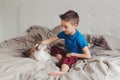 Boy sitting on bed in bedroom at home and petting stroking oriental point-colored cat Royalty Free Stock Photo