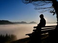 Boy sitting on a bench in the mountains looking down to a fog covered valley. Silhouette of a boy on a sunny day. Royalty Free Stock Photo