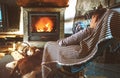 Boy sitting in comfortable armchair in cozy country house near fireplace and enjoying a warm atmosphere and flame moves. His