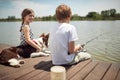 Boy sitting on dock by the river, fishing with his dog and little girl Royalty Free Stock Photo