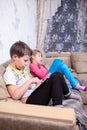 Boy sitting with electronic tablet in hands, girl reading book on couch in room Royalty Free Stock Photo