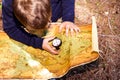 Boy sitting on the forest floor using a compass on an old map