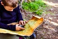 Boy sitting on the forest floor using a compass on an old map