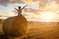 Boy sitting on a hay bale with arms raised in summer watching the sunset Royalty Free Stock Photo