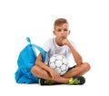 A boy sitting in the lotus position. A sportive kid with bright satchel and soccer ball isolated on a white background.