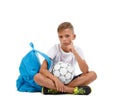 A boy sitting in the lotus position. A sportive kid with bright satchel and soccer ball isolated on a white background.