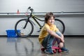 Boy in sitting on penny board and looking at camera, bicycle behind