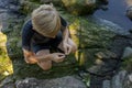 A boy sitting on rocks by the river equips the hook with bait. Sport fishing on the river in summer Royalty Free Stock Photo