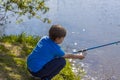 The boy is sitting on the shore of the lake with a fishing rod and fishing. The little fisherman. A child is fishing in the river Royalty Free Stock Photo