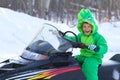 Boy is sitting on a snowmobile and laughing in dragon-like jumpsuit