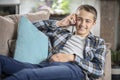 Boy sitting on sofa talking on mobile phone, happy and smiling background Royalty Free Stock Photo