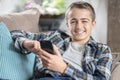 Boy sitting on sofa texting on mobile phone, happy and smiling background Royalty Free Stock Photo