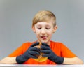 A boy sitting at a table in black disposable gloves holds in front of him a huge burger sprinkled with sesame seeds a boy looking Royalty Free Stock Photo