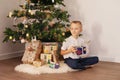 The boy is sitting under the Christmas tree with a gift in his hands happy Royalty Free Stock Photo